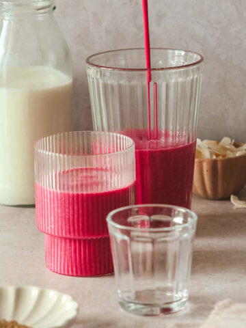 pink breakfast smoothie poured into glassed on beige-pink backdrop with props.