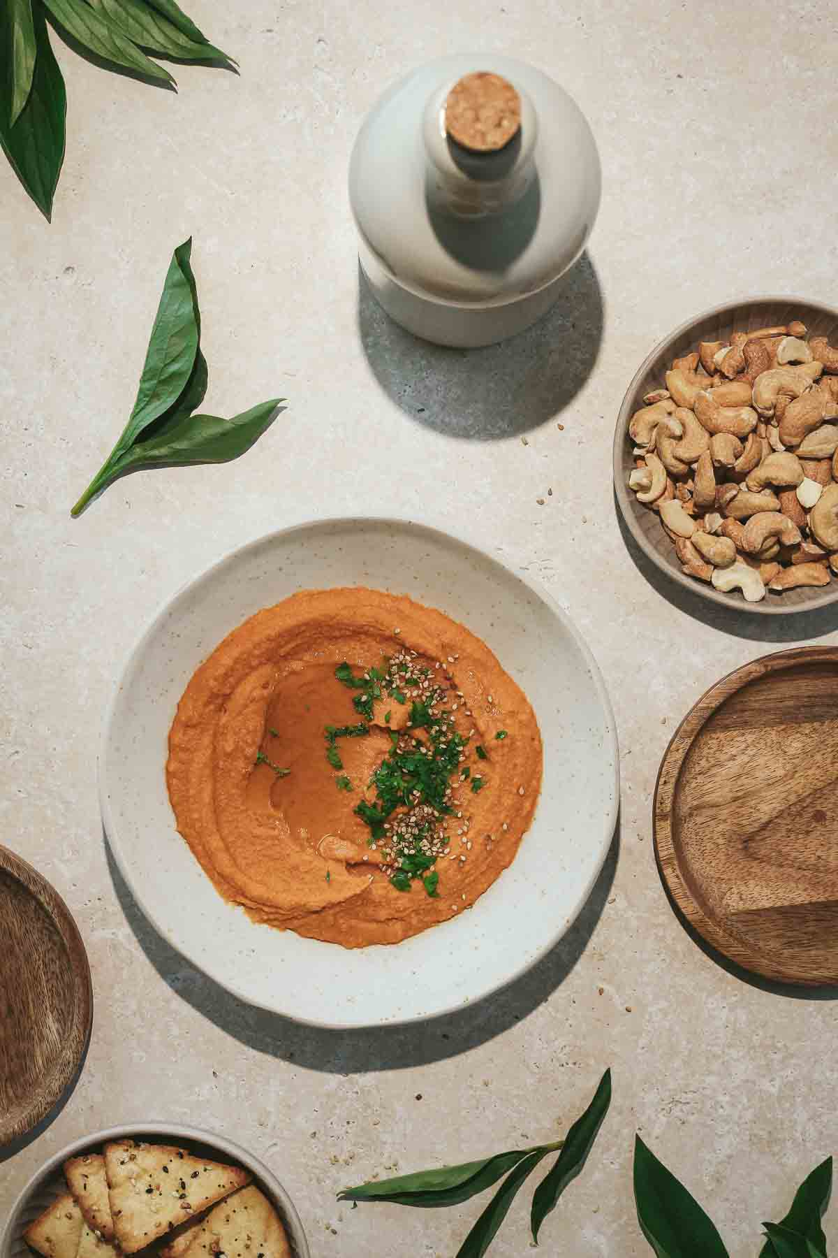 moroccan spiced hummus in beige bowl with crackers and nuts on beige marble background.