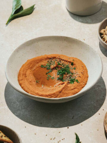 moroccan spiced hummus in beige bowl with crackers and nuts on beige marble background.