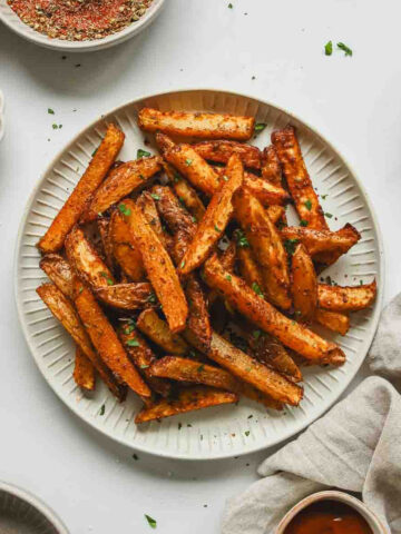 cajun style fries on white plate with parsley sprinkled on.