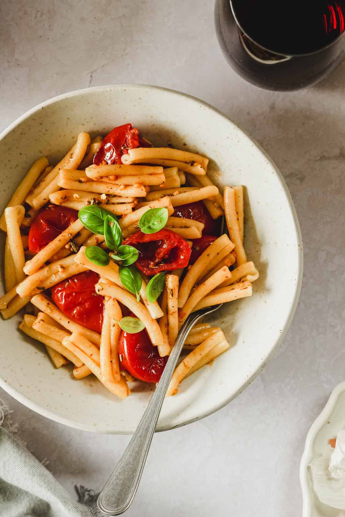 oven roasted tomato pasta on beige marble background with glass of red wine.