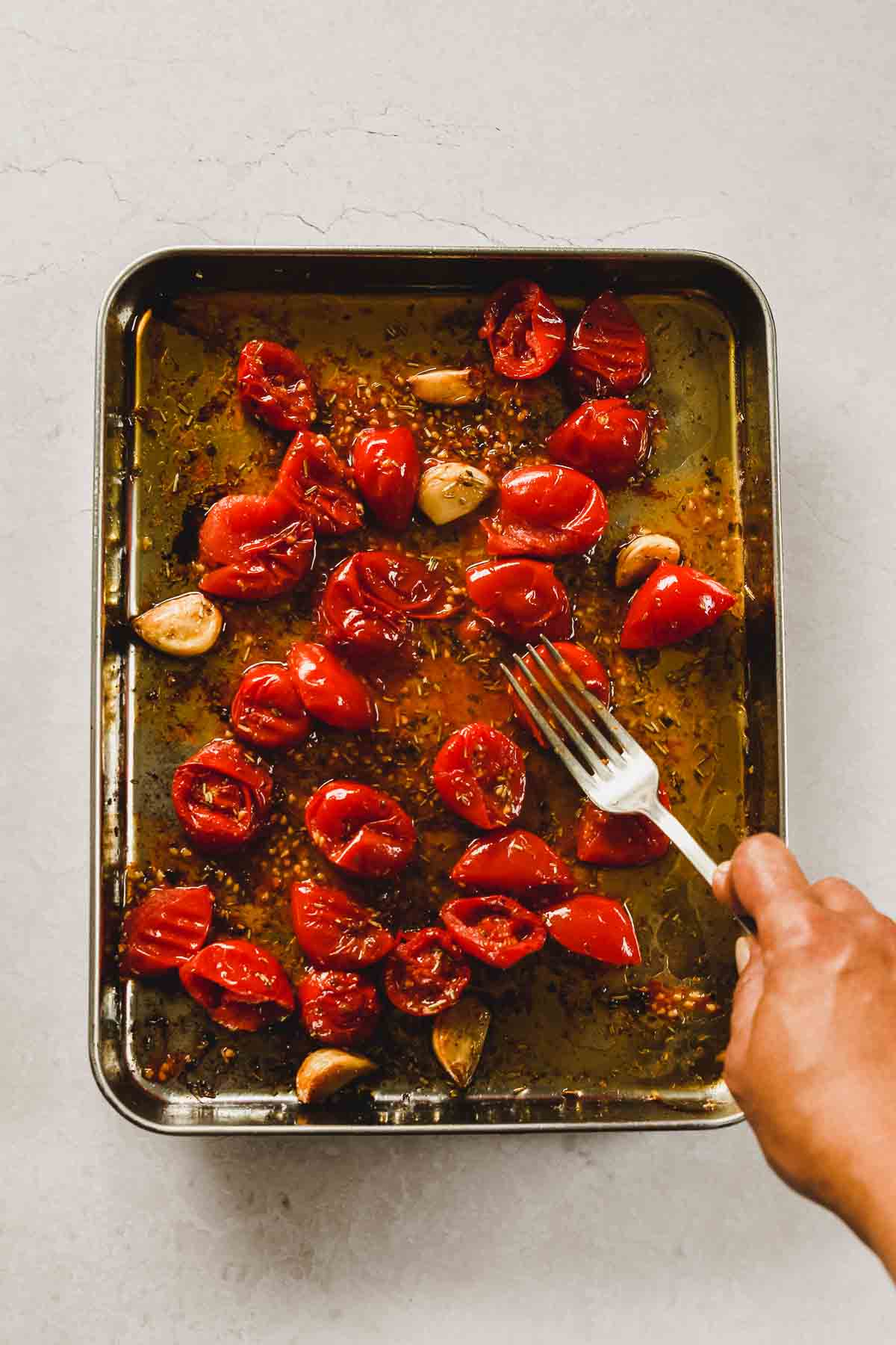 smashing roasted cherry tomatoes with fork on sheet pan.