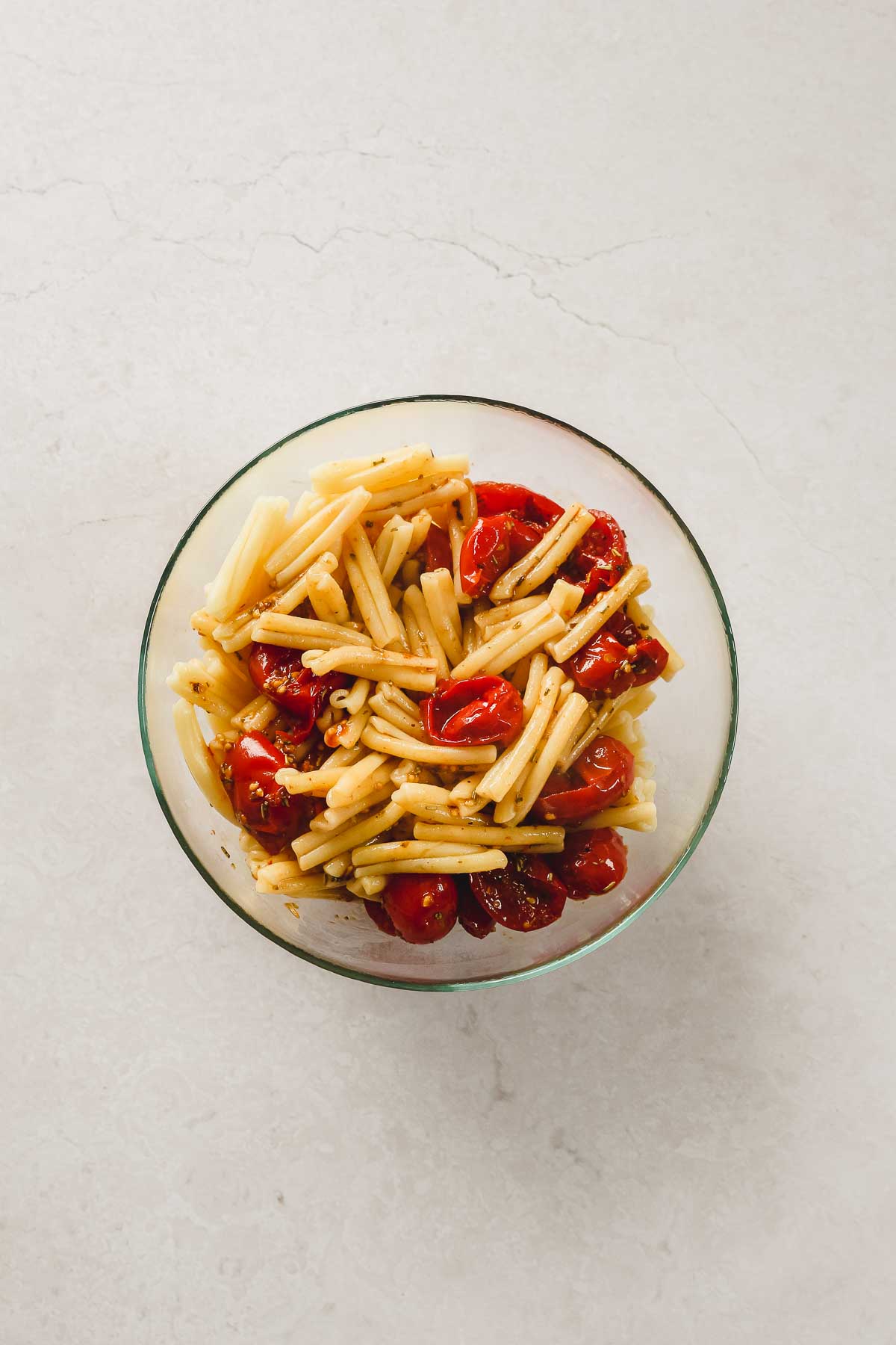 mixing roasted cherry tomatoes with casarecce pasta in glass bowl.