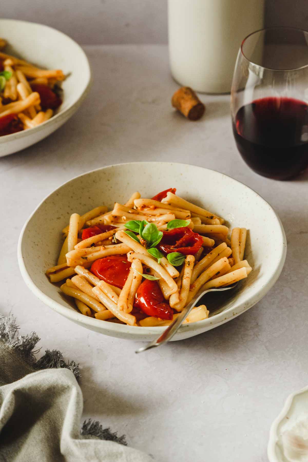 cherry tomato pasta with basil in beige bowl with vintage fork and props.