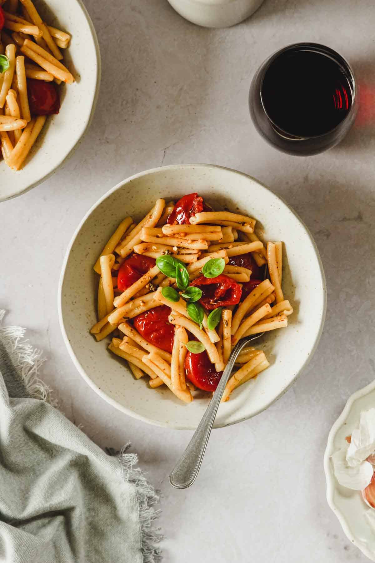 roasted cherry tomato pasta in beige bowl with vintage fork an props.