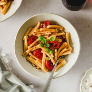 oven roasted cherry tomato pasta with basil in beige bowl with vintage fork and props.