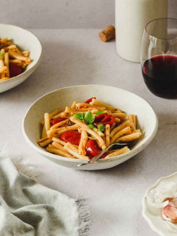 cherry tomato pasta with basil in beige bowl with vintage fork and props.