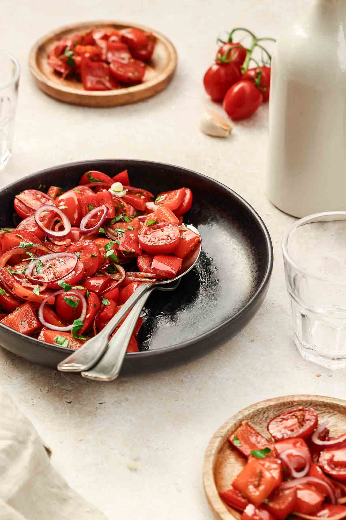 close up of roasted red pepper salad with cherry tomatoes and red onion on black plate with vintage cutlery.