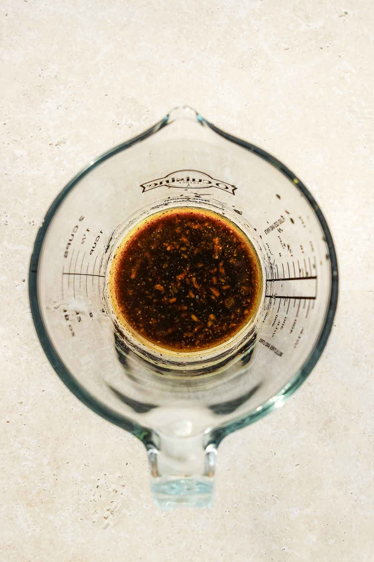 balsamic vinegar dressing in glass measuring cup on beige background.