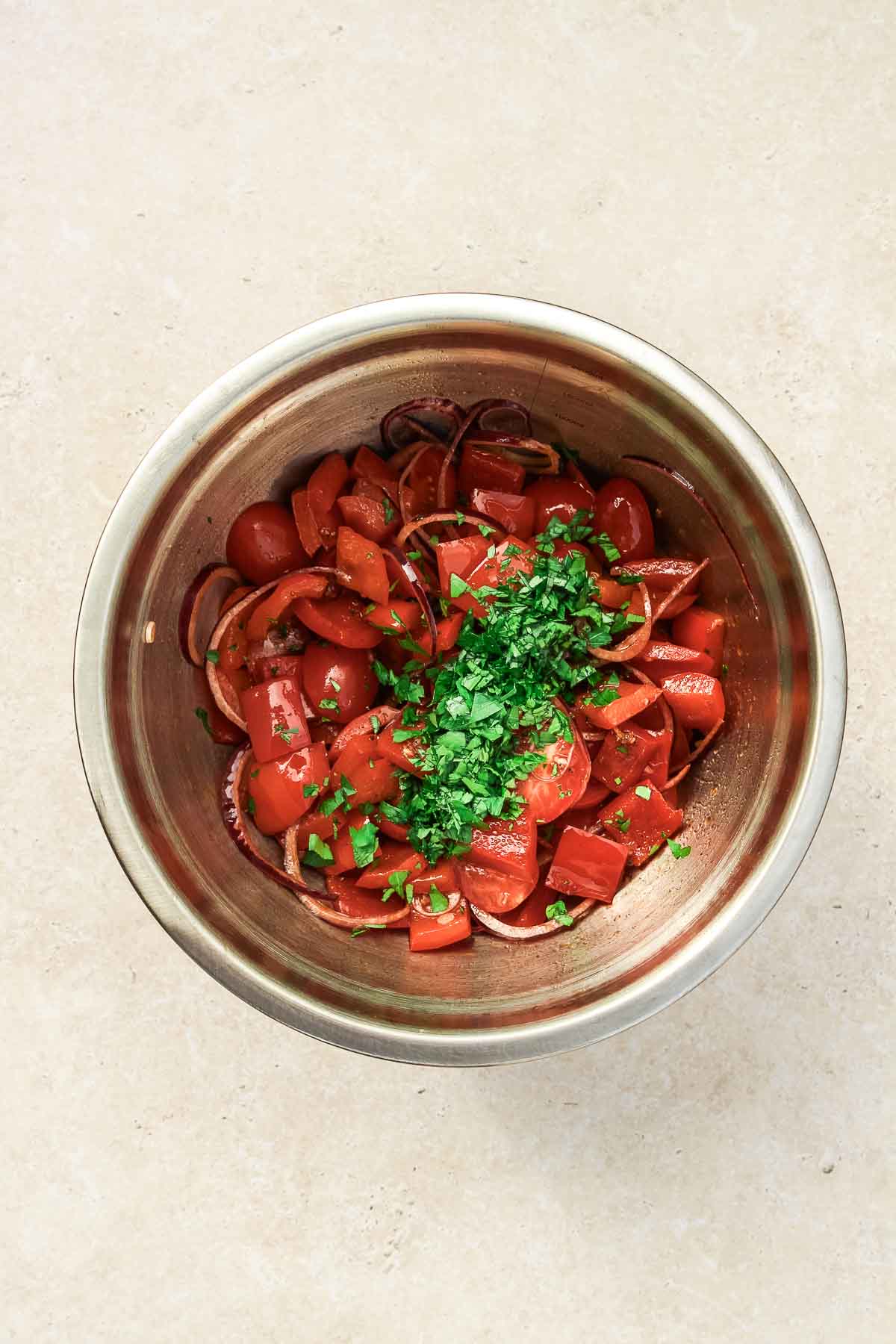 mixing ingredients for roasted red bell pepper salad in metal bowl on beige background.