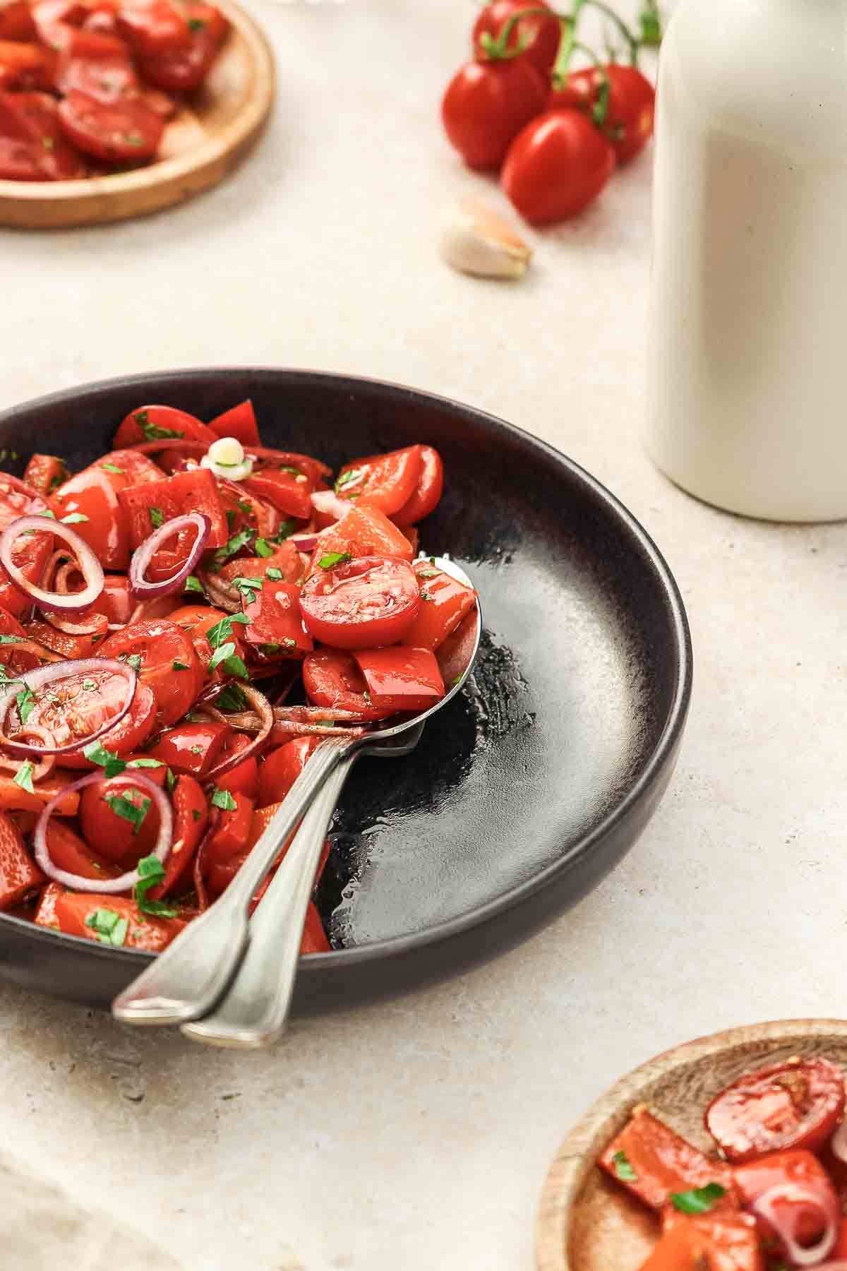 close up of roasted red pepper salad with cherry tomatoes and red onion on black plate with vintage cutlery.