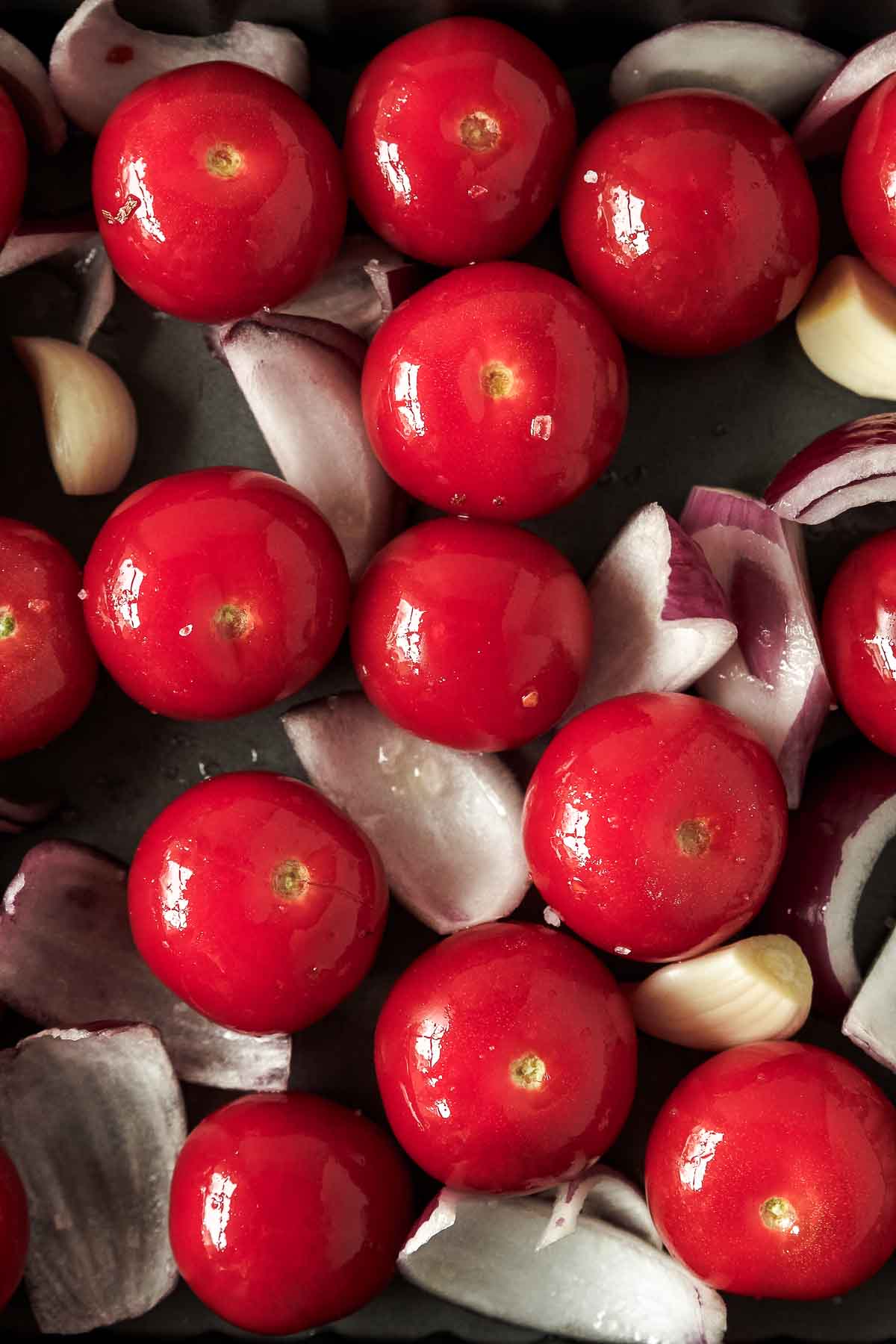 close up of seasoned tomatoes, red onion and garlic in baking dish before roasting.