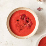 homemade roasted tomato soup in beige speckled bowl on beige background.