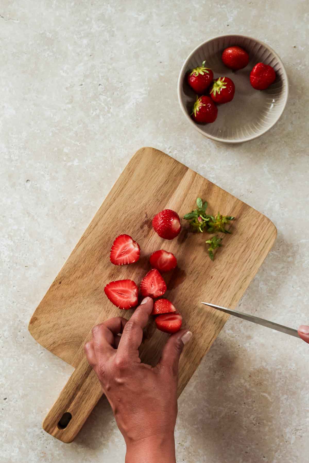 slicing strawberries in half on wooden cutting board.