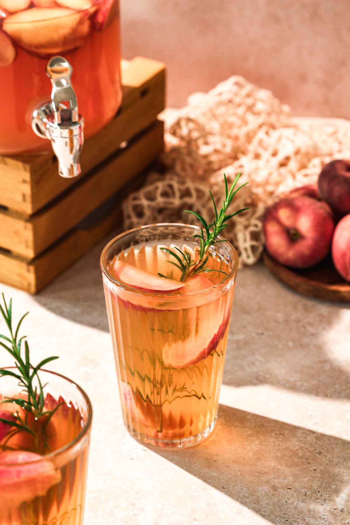 diy peach iced tea with rosemary garnish and props in background.