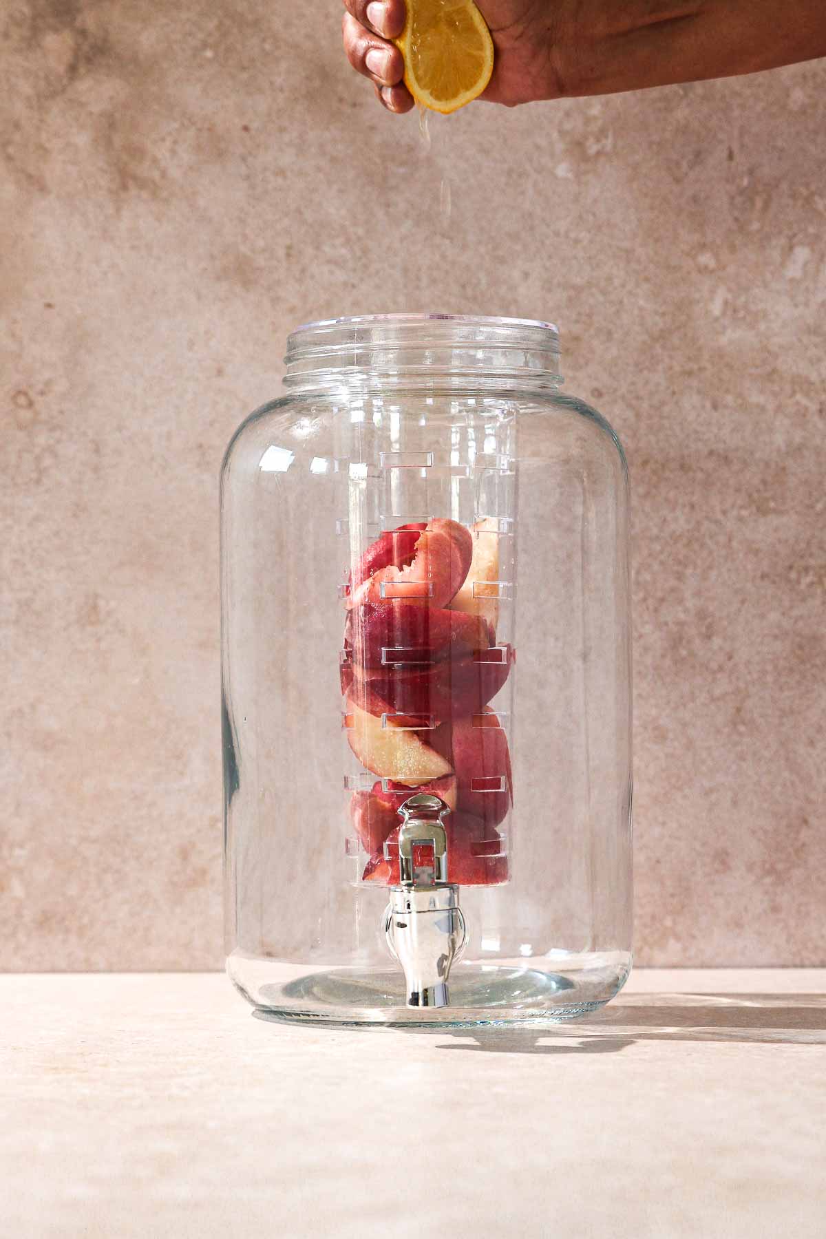 squeezing lemon into beverage dispenser with peaches for iced tea.