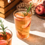 homemade healthy peach iced tea with rosemary garnish and fresh peaches.