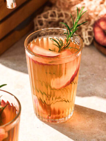 homemade healthy peach iced tea with rosemary garnish and fresh peaches.