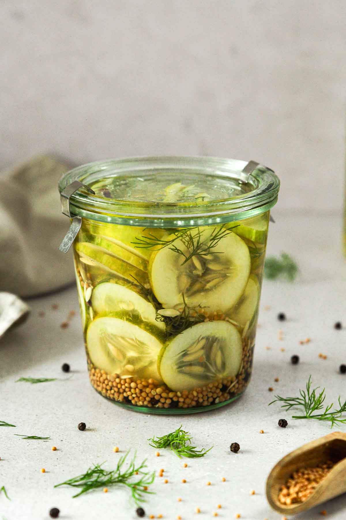 sweet and sour pickled cucumber sin glass jar with herbs and spices scattered around.