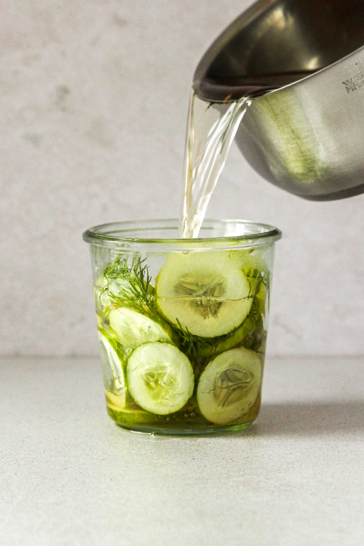 pouring infused vinegar into weck jar with cucumber slices and dill.