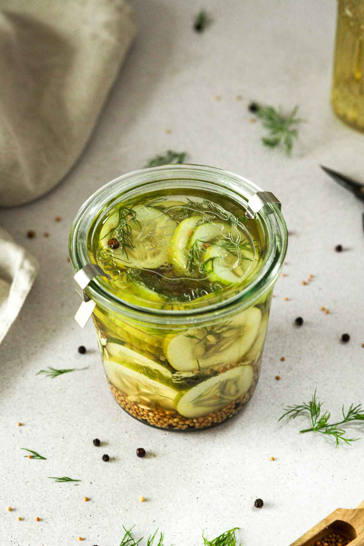 pickled cucumber slices in weck jar on grey background with props.