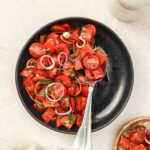 sweet pepper salad on black plate with vintage cutlery on beige background.