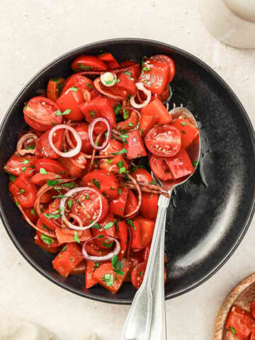 sweet pepper salad on black plate with vintage cutlery on beige background.