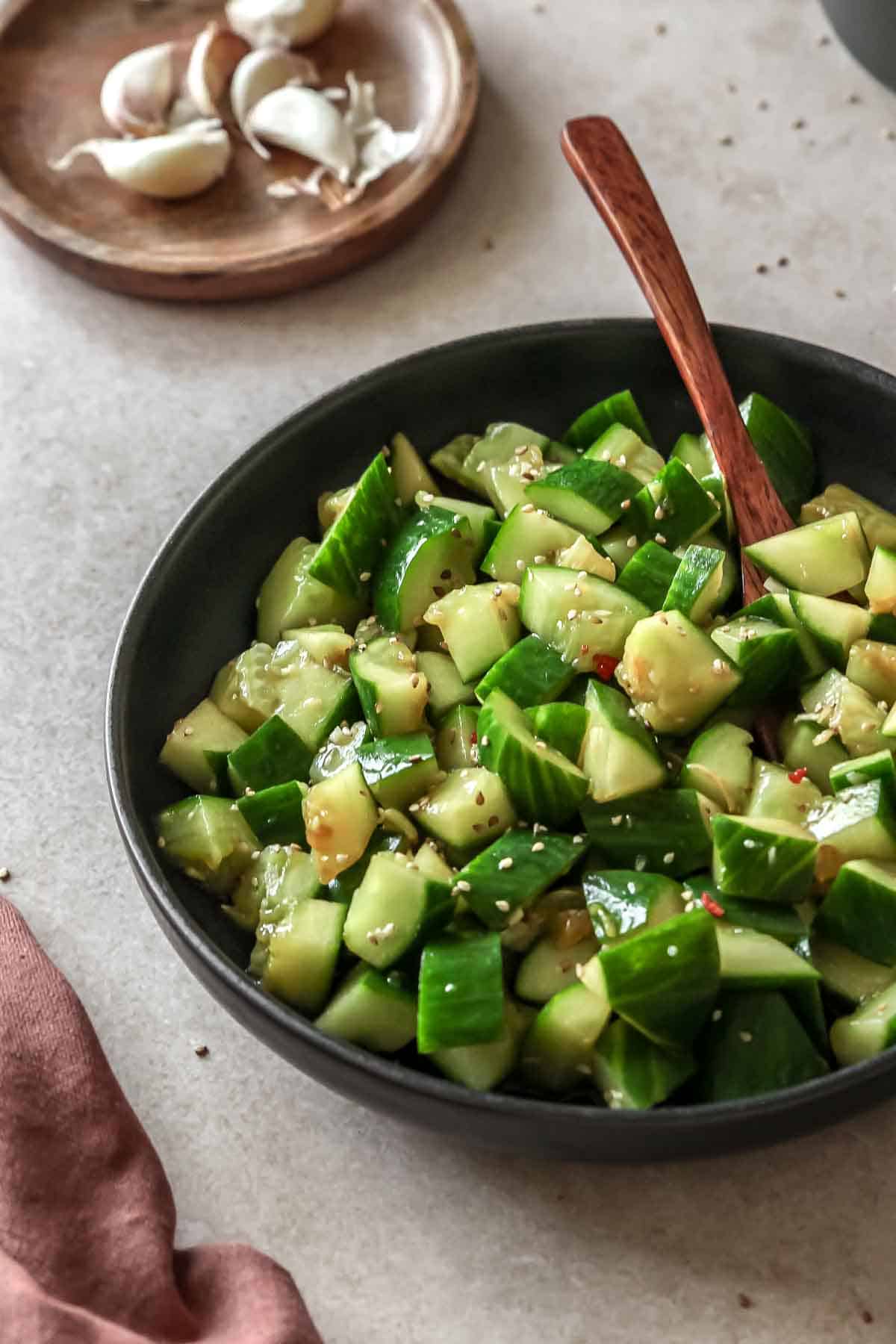 asian cucumber salad on black bowl with wooden spoon on beige background.