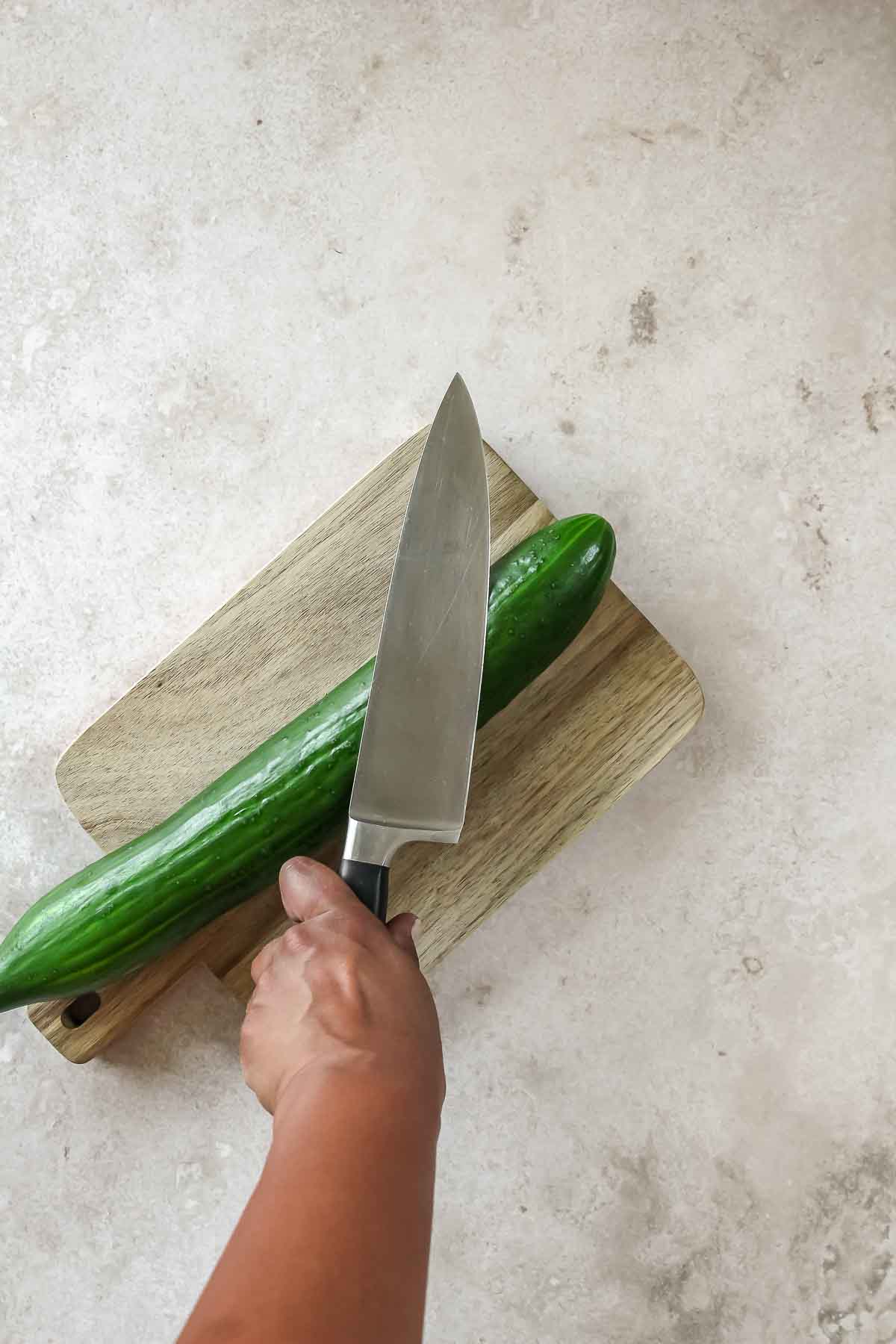 smashing cucumber with big knife on wooden board.