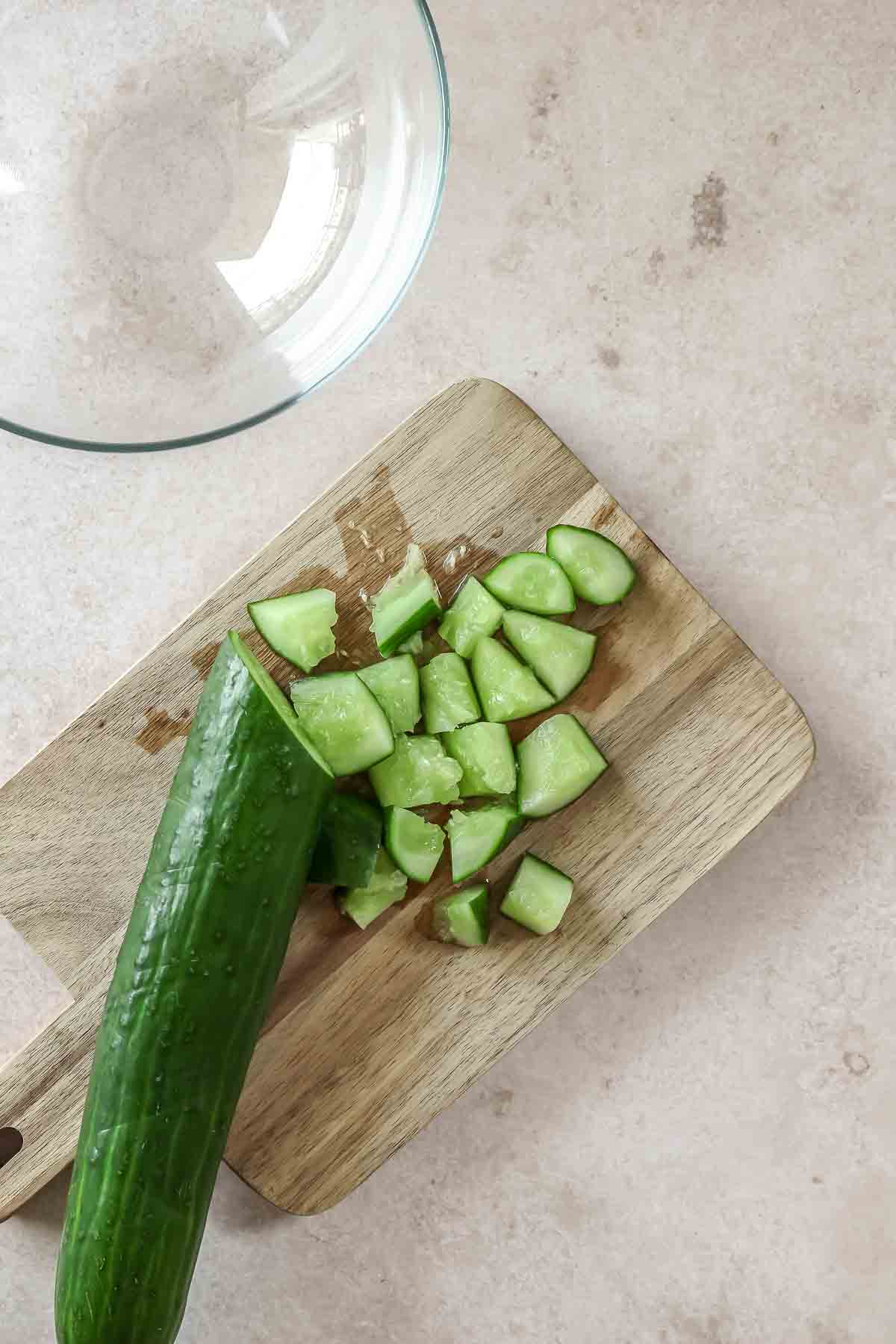 chopped cucumber on wooden chopping board.