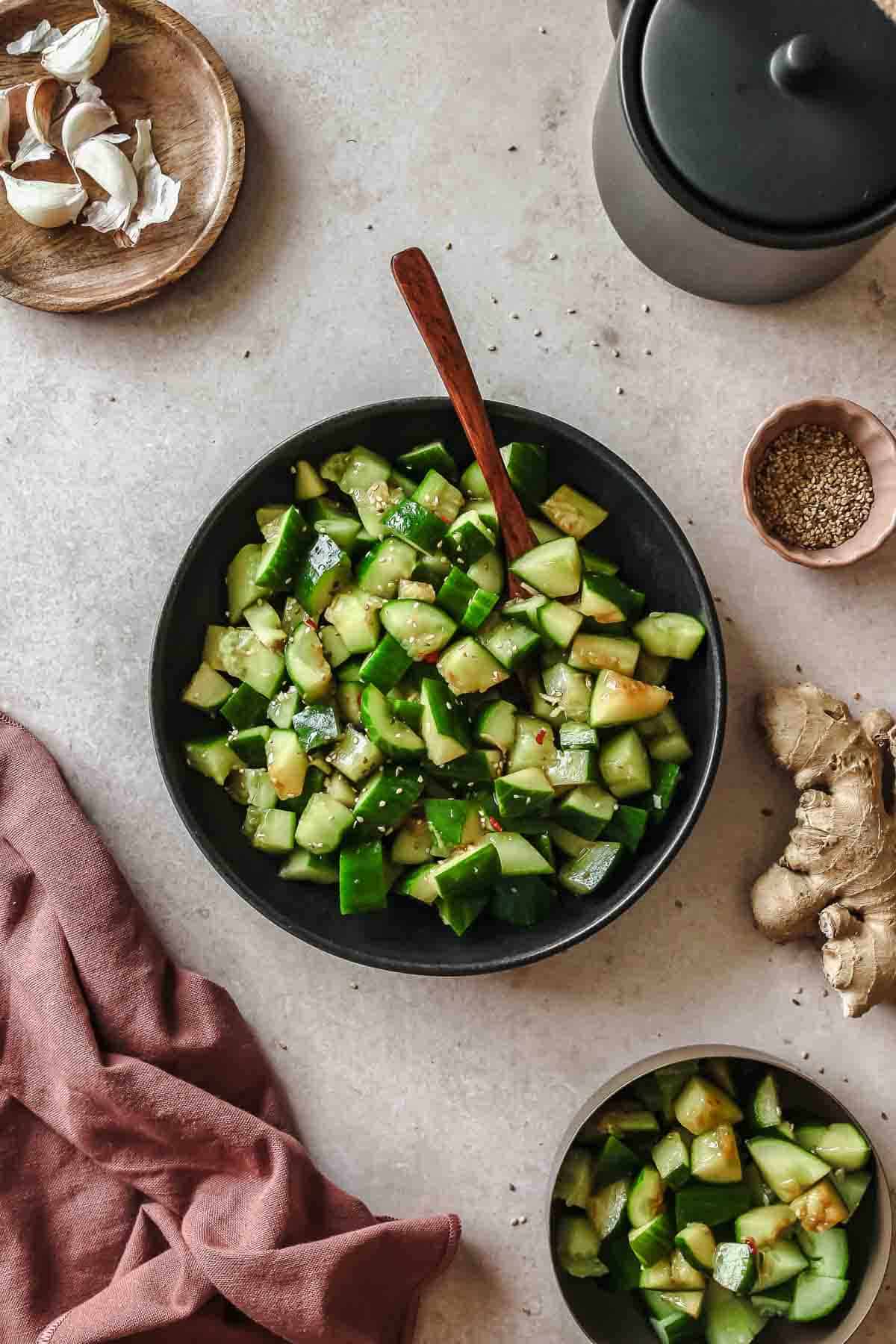 spicy asian smashed cucumber salad on black plate with wooden spoon and props.