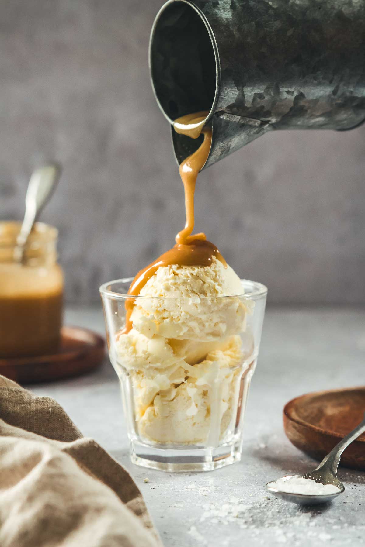 pouring vegan caramel over vanilla ice cream in glass on grey background.