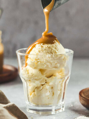 pouring vegan caramel over vanilla ice cream in glass on grey background.