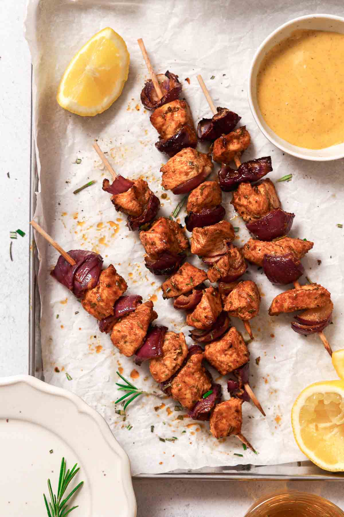 air fryer chicken skewers with red onion on baking sheet with parchment paper, sauce and lemons.