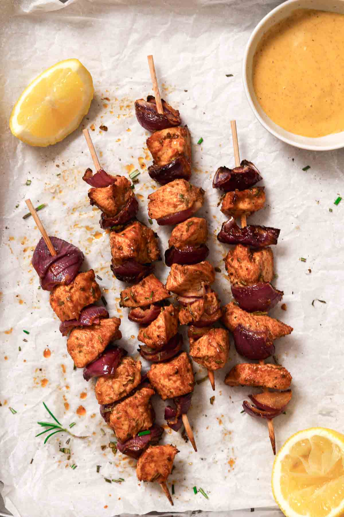 air fryer chicken skewers with red onion on baking sheet with parchment paper, sauce and lemons.