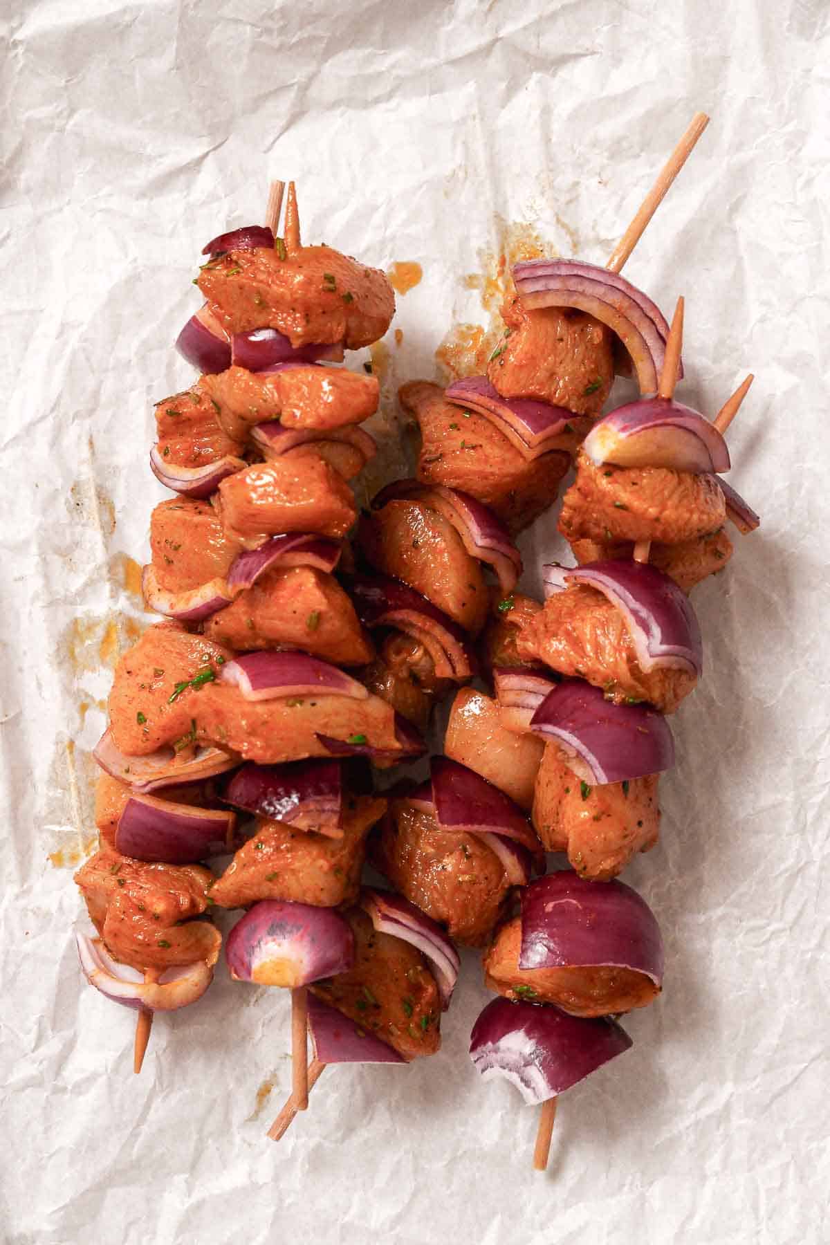 marinated chicken with red onion on wooden skewers.