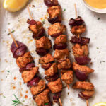 chicken kabobs with red onion on parchment paper with rosemary garnish.