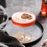 aperol sour aperitif with frothy finish and dried orange slice garnish on vintage plate.