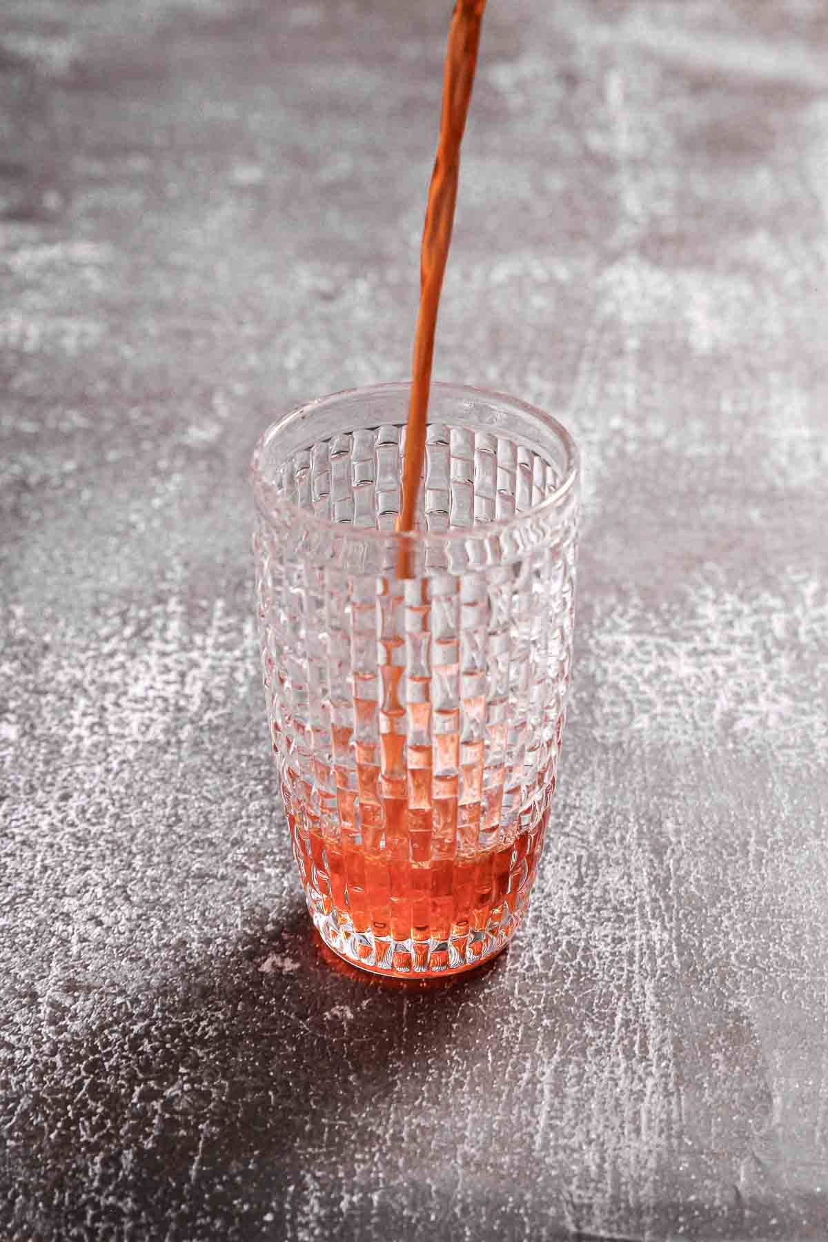 pouring aperol into glass cocktail shaker.