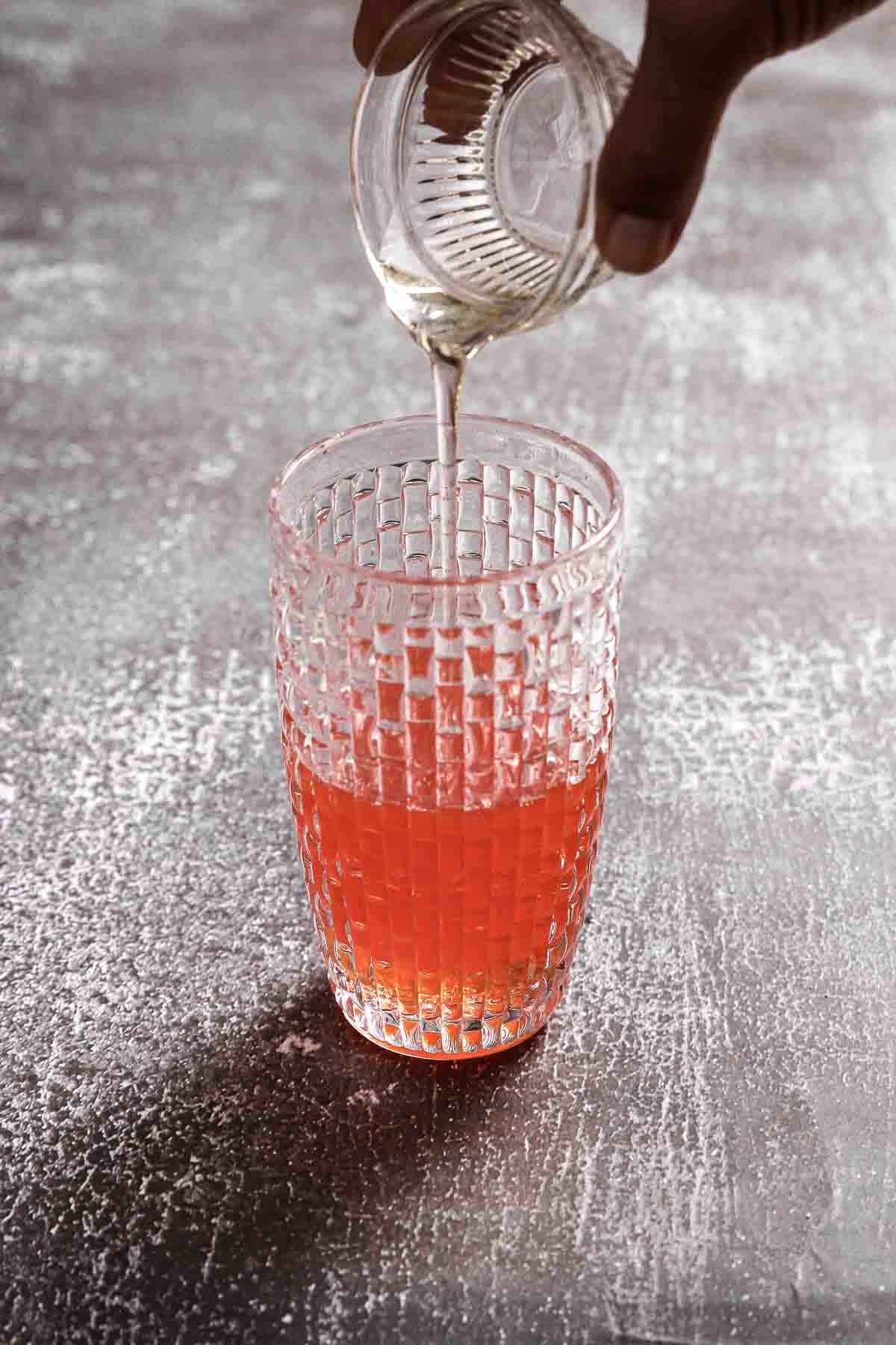 pouring agave syrup into cocktail shaker with Aperol and lemon juice.