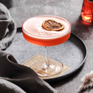 aperol sour aperitif with frothy finish and dried orange slice garnish on vintage plate.