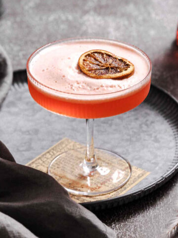 aperol sour aperitif with frothy finish and dried orange slice garnish on vintage plate.