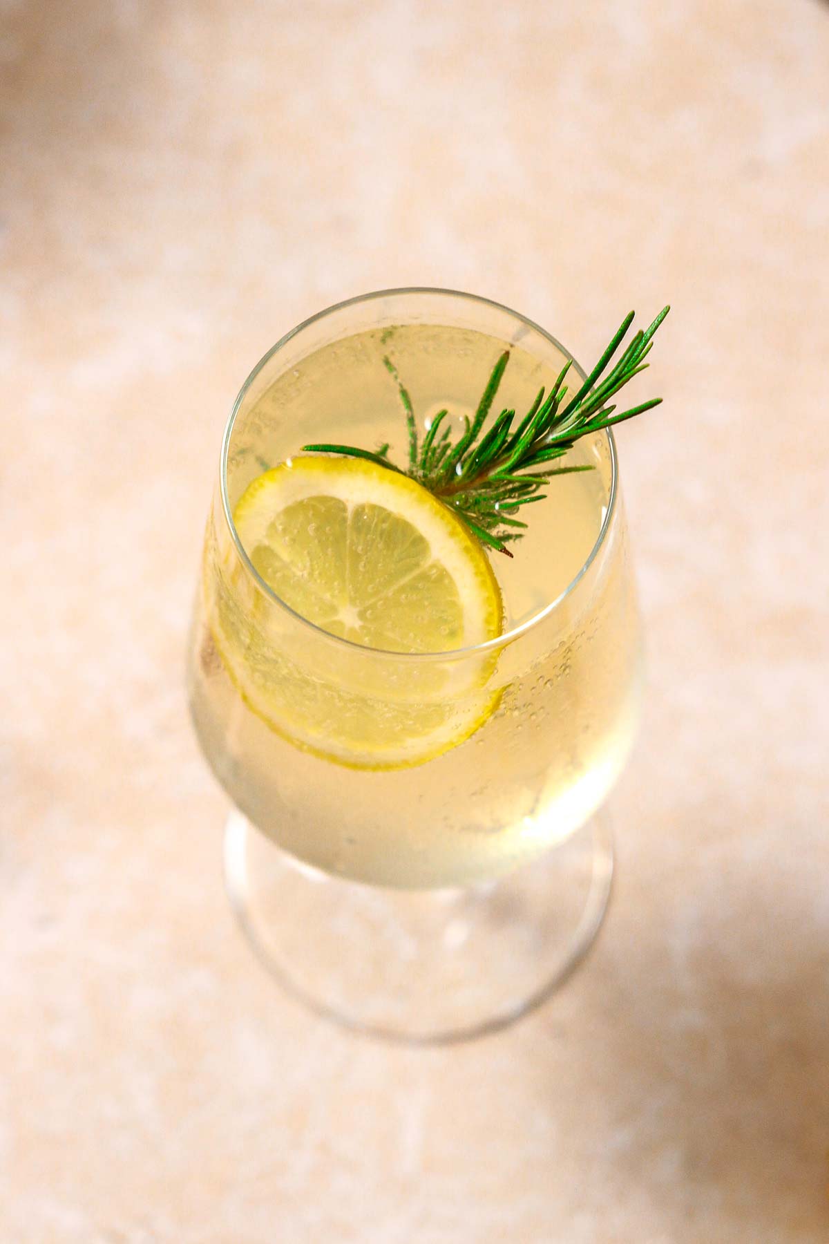 limoncello spritz on beige background with rosemary and lemon garnish.