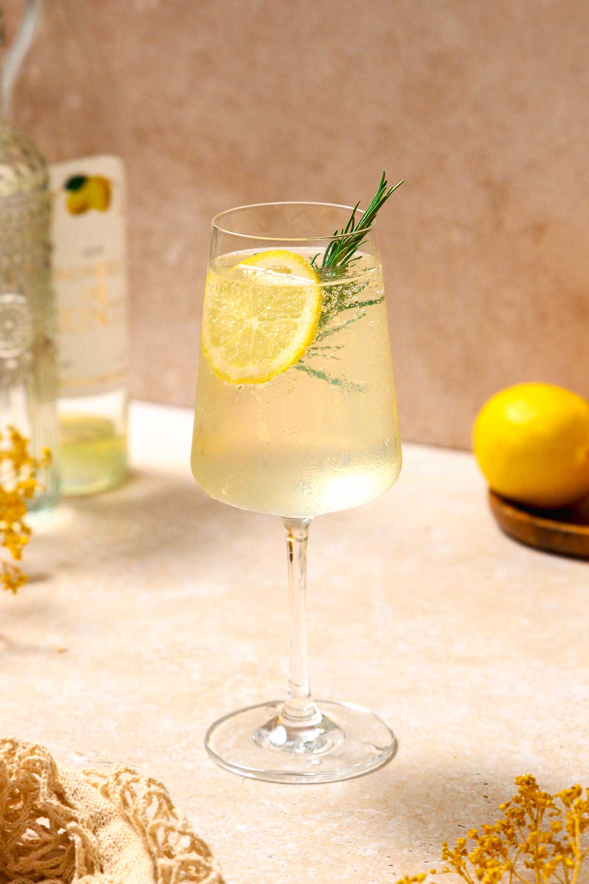 limoncello spritz cocktail with lemon and rosemary garnish on beige marble background.