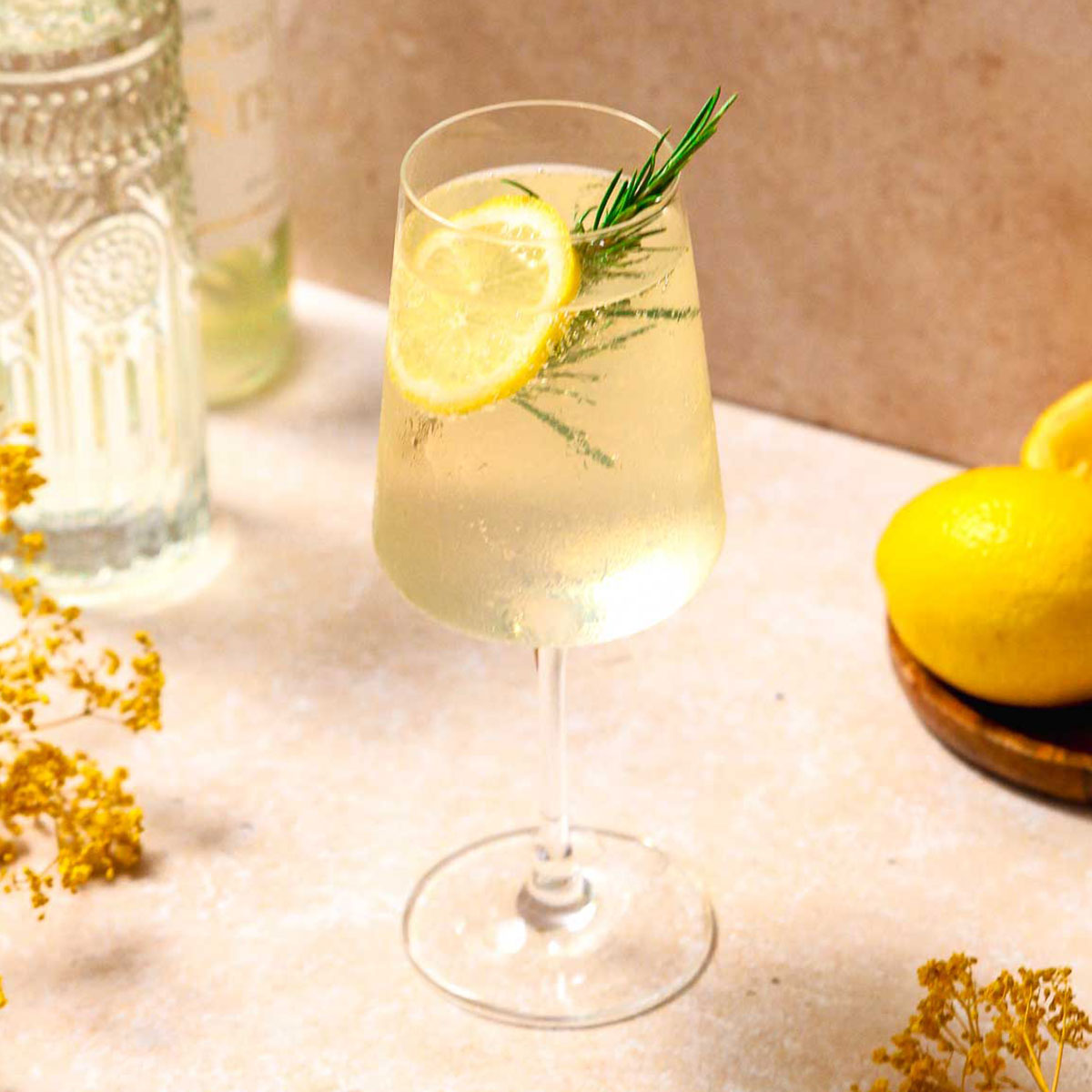 limoncello spritz cocktail with lemon and rosemary garnish on beige marble background.