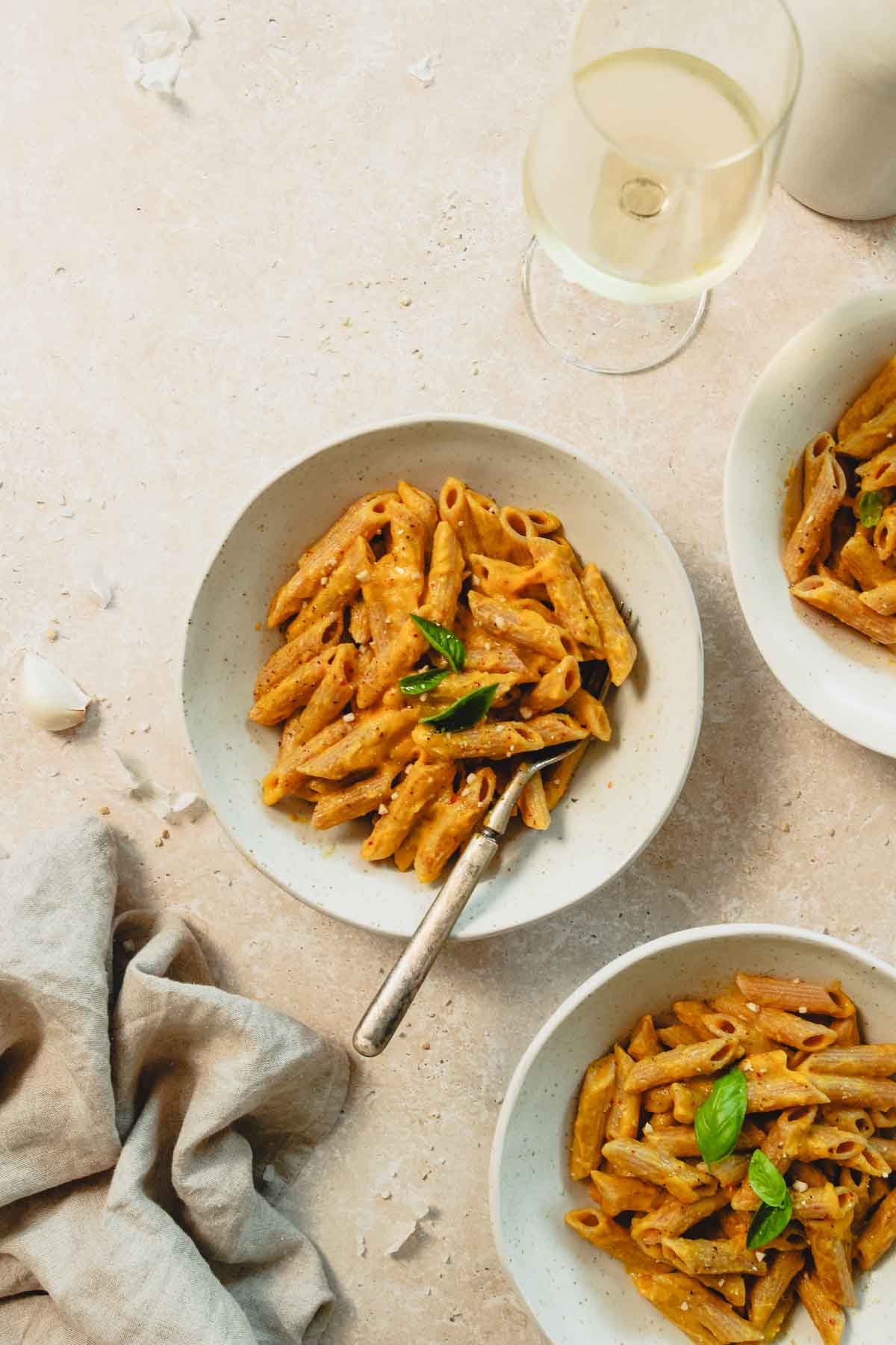 roasted pumpkin pasta sauce in beige bowls with vintage fork on beige marble background.