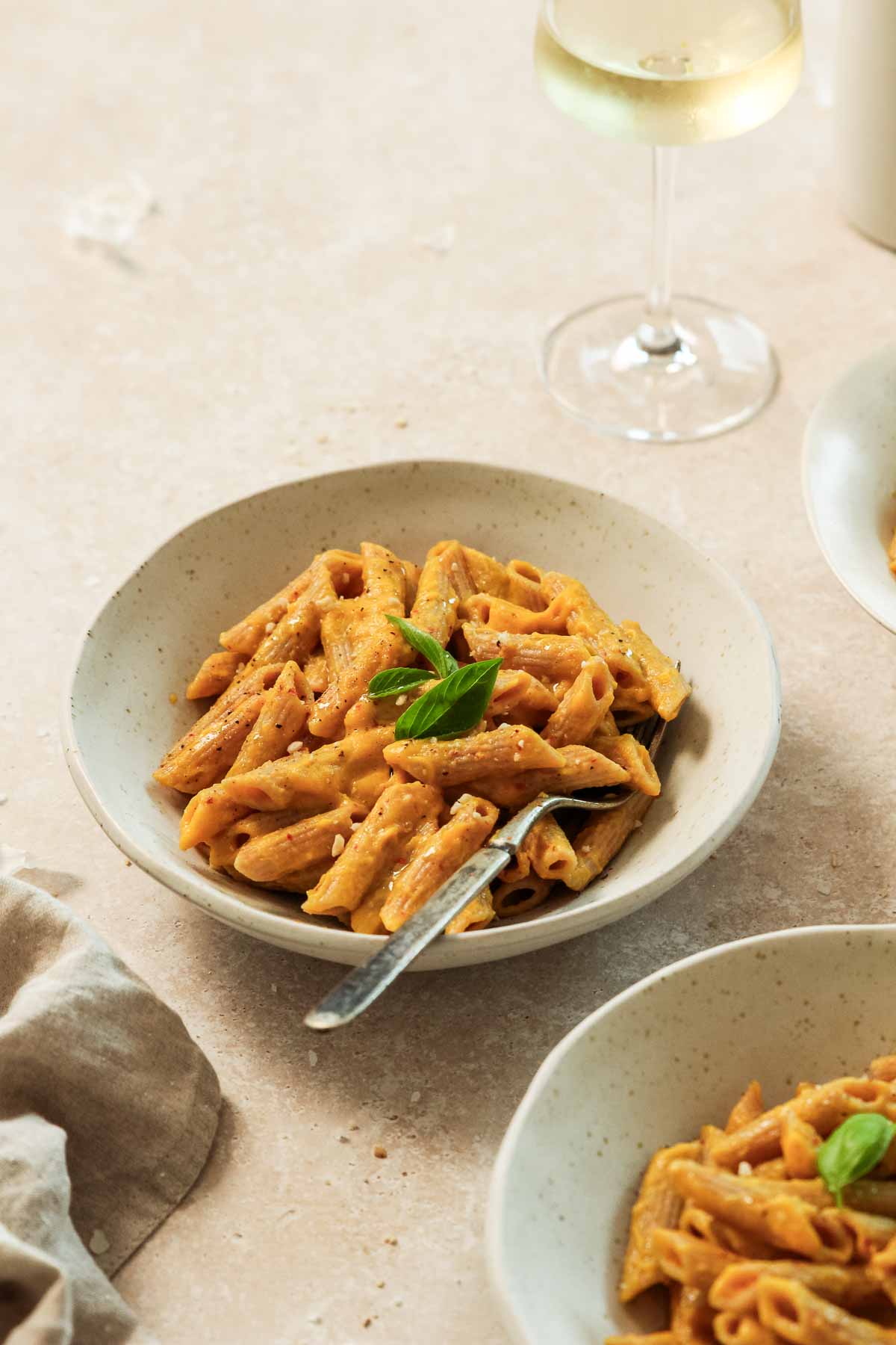 roasted pumpkin pasta sauce in beige bowls with vintage fork on beige marble background.