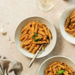 roasted pumpkin pasta sauce in beige bowls with vintage fork on beige marble background.