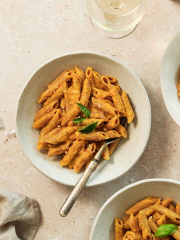 roasted pumpkin pasta sauce in beige bowls with vintage fork on beige marble background.