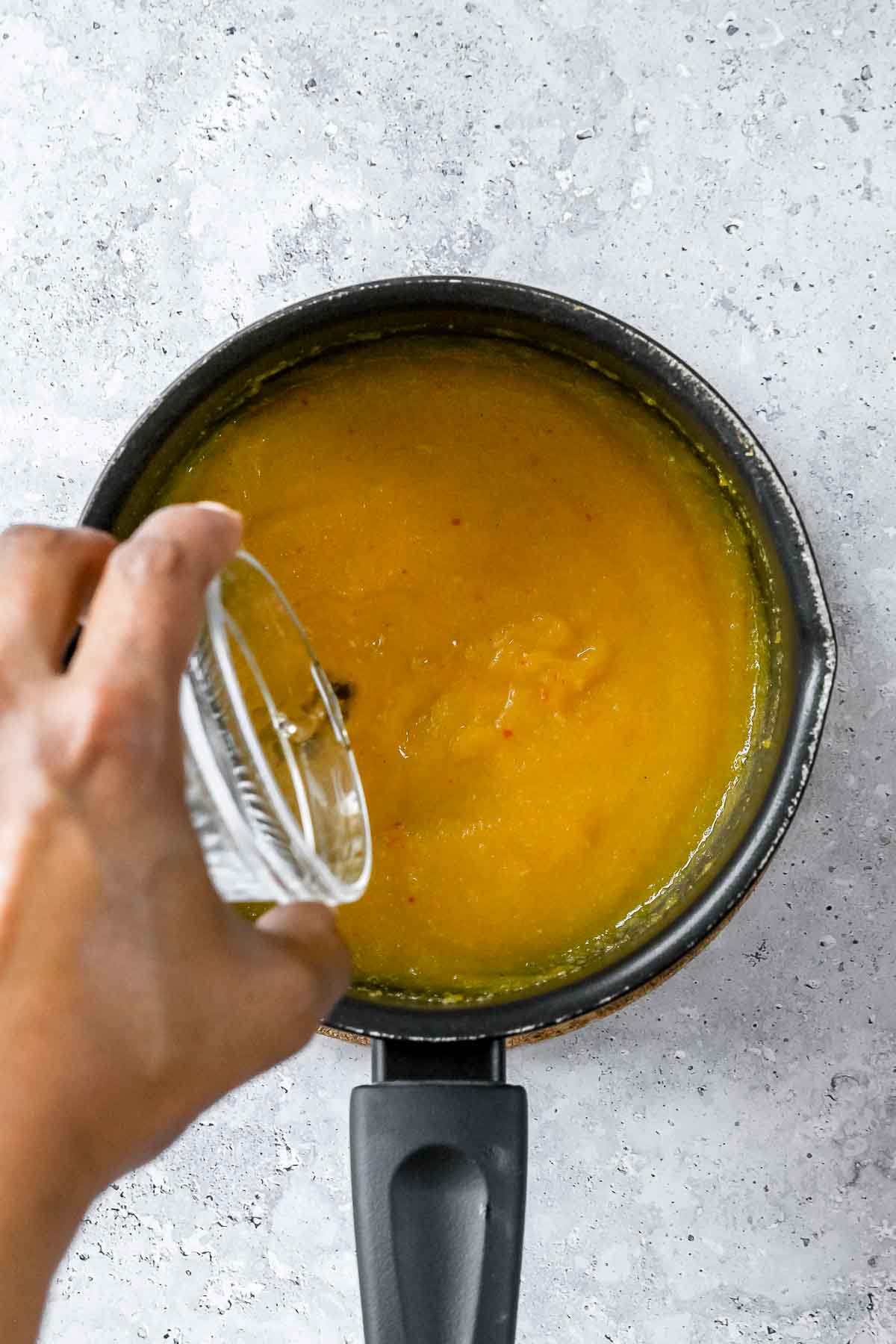 pouring apple cider vinegar into cooking mango sauce.